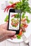 Hands taking photo vegetable salad with meat with smartphone