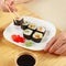 Hands taking sushi with chopsticks. Assorted sushi with ginger and wasabi on bamboo mat.