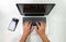 Hands typing a light colored computer with a cell phone aside on a white desk