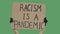 The hands of an unknown person in black gloves raise a cardboard poster RACISM IS A PANDEMIC. Equality and unity concept