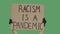 Hands of an unknown person in black gloves raise cardboard poster RACISM IS A PANDEMIC. Stop Racism concept, No Racism