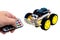 Hands using a wireless remote turn on a programmable robotic car with the ability to avoid obstacles and the ability to follow a