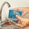 Hands wash the dirty glass under running water in kitchen