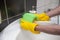 Hands wearing yellow glowes cleaning the faucet of a sink in bathroom