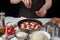 Hands of the woman cook sprinkle Italian raw pizza margarita oreano on a dark background. On the white table lie the ingredients o