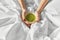 Hands of woman with cup of matcha tea in bed