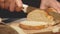 Hands of a woman cutting bread loaf on wooden cutting board