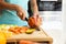 Hands of a woman cutting some vegetables and fruits in wooden table in the kitchen.