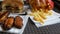 Hands of a woman take french fries. Burgers, chicken wings, french fries on tray in a fast food restaurant. Unhealthy