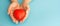 In the hands of a woman is a toy red small heart on a blue background, a banner, copyspace on the right.