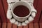 Hands in woolen warm gloves holding cup of hot black tea against unfocused orange bench top view.