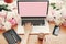 Hands working on stylish laptop with empty screen, coffee cup, notebook,phone, pink and white peonies on wooden table with space