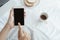 Hands working woman holding and using smart phone on desk background. On the desk have cup coffee, breads and laptop