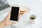 Hands of working woman holding and using smart phone on desk background. On the desk have cup coffee, breads and laptop