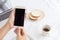 Hands of working woman holding and using smart phone on desk background. On the desk have cup coffee, breads and laptop