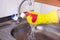 Hands in yellow gloves clean sink with sponge and a special cleaning agent, detergent spray. Hygiene in the kitchen, cleaning the