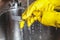 Hands in yellow rubber gloves wash plug in sink