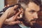 The hands of young barber making haircut to attractive man in barbershop