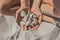 The hands of a young girl hold a bunch of shells sitting on the beach sand close up