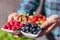 The hands of a young man hold a white plate with a mixture of fresh berries