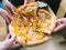 Hands of young people taking pizza slices from delivery cardboard box dining together, friends sharing meal having lunch at home