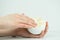 Hands of young woman holding the hand care cream and putting fingers in it, on white background.