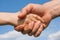 Handshake of a child and an adult against a blue sky