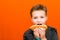 Handsome 10 yers old boy holding and biting hot dog closeup indoors orange studio background image.Close up,copy space