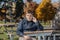 handsome adolescent boy sitting in sunny warm park and communicating on cellphone against natural autumn background