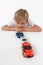 Handsome adorable little boy lying behind a line of car toys with arms crossed and seeming bored