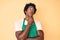 Handsome african american man with afro hair wearing waiter apron serious face thinking about question with hand on chin,