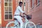 Handsome African American man stylish well-dressed standing with a blue bicycle red brick building background . sports