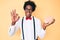 Handsome african american nerd man with afro hair holding brain doing ok sign with fingers, smiling friendly gesturing excellent