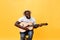 Handsome african american retro styled guitarist playing acoustic guitar isolated on yellow background.