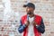 Handsome African man in casual clothes and a cap is standing in slum on background of ruined red brick wall