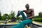 Handsome afro American sportman sitting on the street while taking break after training. Black male having rest after