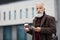 Handsome aged man holding coffee and using smartphone