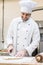 Handsome baker smiling and cutting uncooked dough