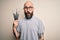 Handsome bald artist man with beard and tattoo painting using painter brushes scared in shock with a surprise face, afraid and