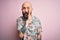 Handsome bald man with beard and tattoo wearing casual floral shirt over pink background hand on mouth telling secret rumor,