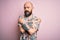 Handsome bald man with beard and tattoo wearing casual floral shirt over pink background Hugging oneself happy and positive,