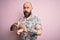 Handsome bald man with beard and tattoo wearing casual floral shirt over pink background In hurry pointing to watch time,