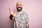 Handsome bald man with beard and tattoo wearing casual floral shirt over pink background smiling friendly offering handshake as