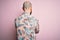 Handsome bald man with beard and tattoo wearing casual floral shirt over pink background standing backwards looking away with