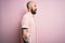 Handsome bald man with beard and tattoo wearing casual shirt over isolated pink background looking to side, relax profile pose