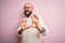 Handsome bald man with beard and tattoo wearing glasses and sweater over pink background disgusted expression, displeased and