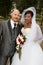 Handsome bald man in black suit and beautiful african american woman with dark curly hair in white dress with bouquet of flowers l