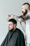 handsome barber drying customer hair with hairdryer at barbershop