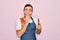 Handsome barber man with blue eyes wearing apron using razor blade over pink background cover mouth with hand shocked with shame