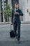 Handsome bearded businessman in classic suit with suitcase is looking at his watch